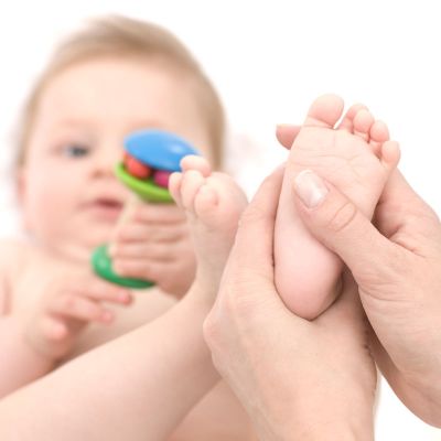 Hand hält Babyfuß, Baby spielt mit Spielzeug
